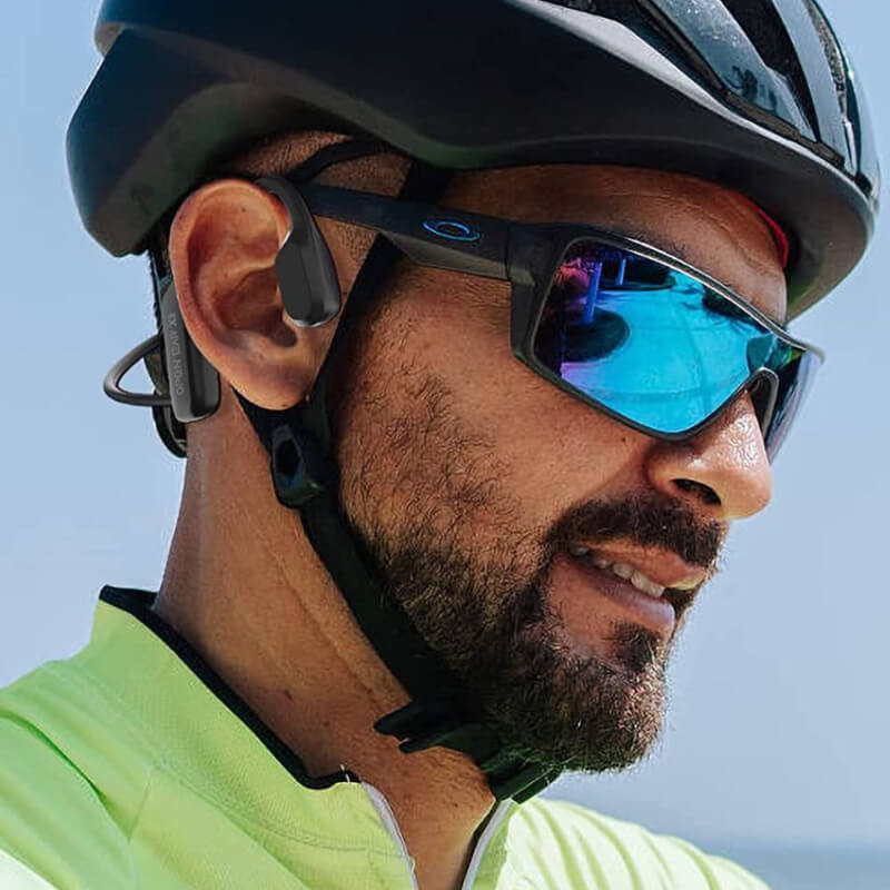 Man wearing wireless bone conduction headphones and sunglasses while cycling outdoors.