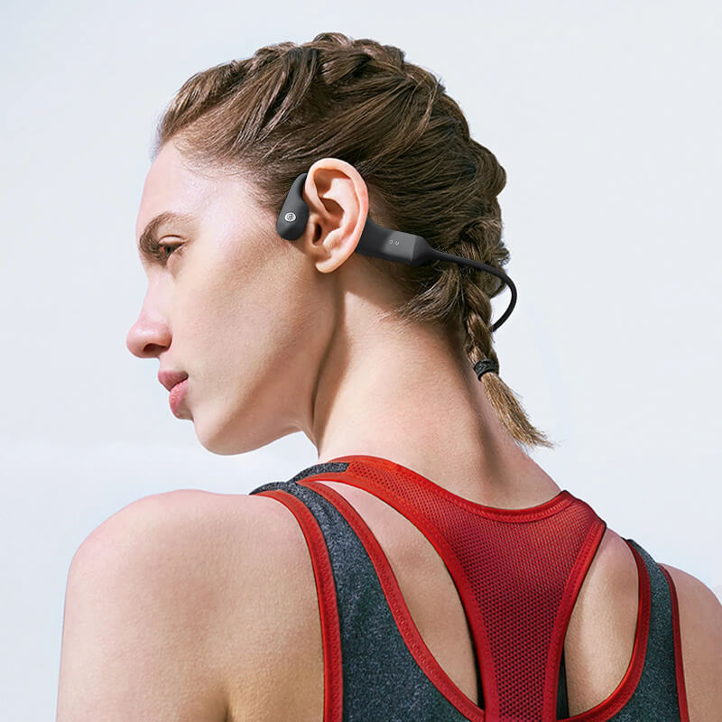 Wireless bone conduction headphones worn by a woman with braided hair in athletic apparel.