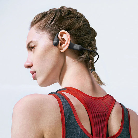 Wireless bone conduction headphones worn by a woman with braided hair in athletic apparel.